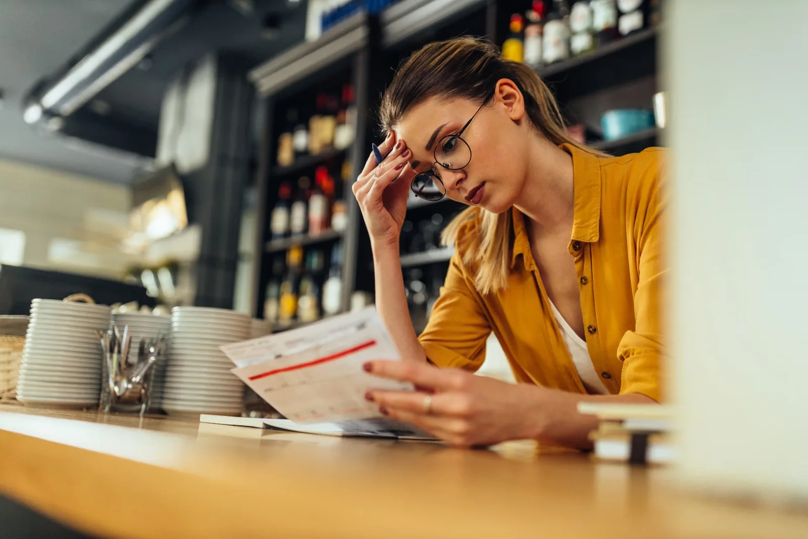 Concerned restaurant owner at her counter reviewing printed bills and reports